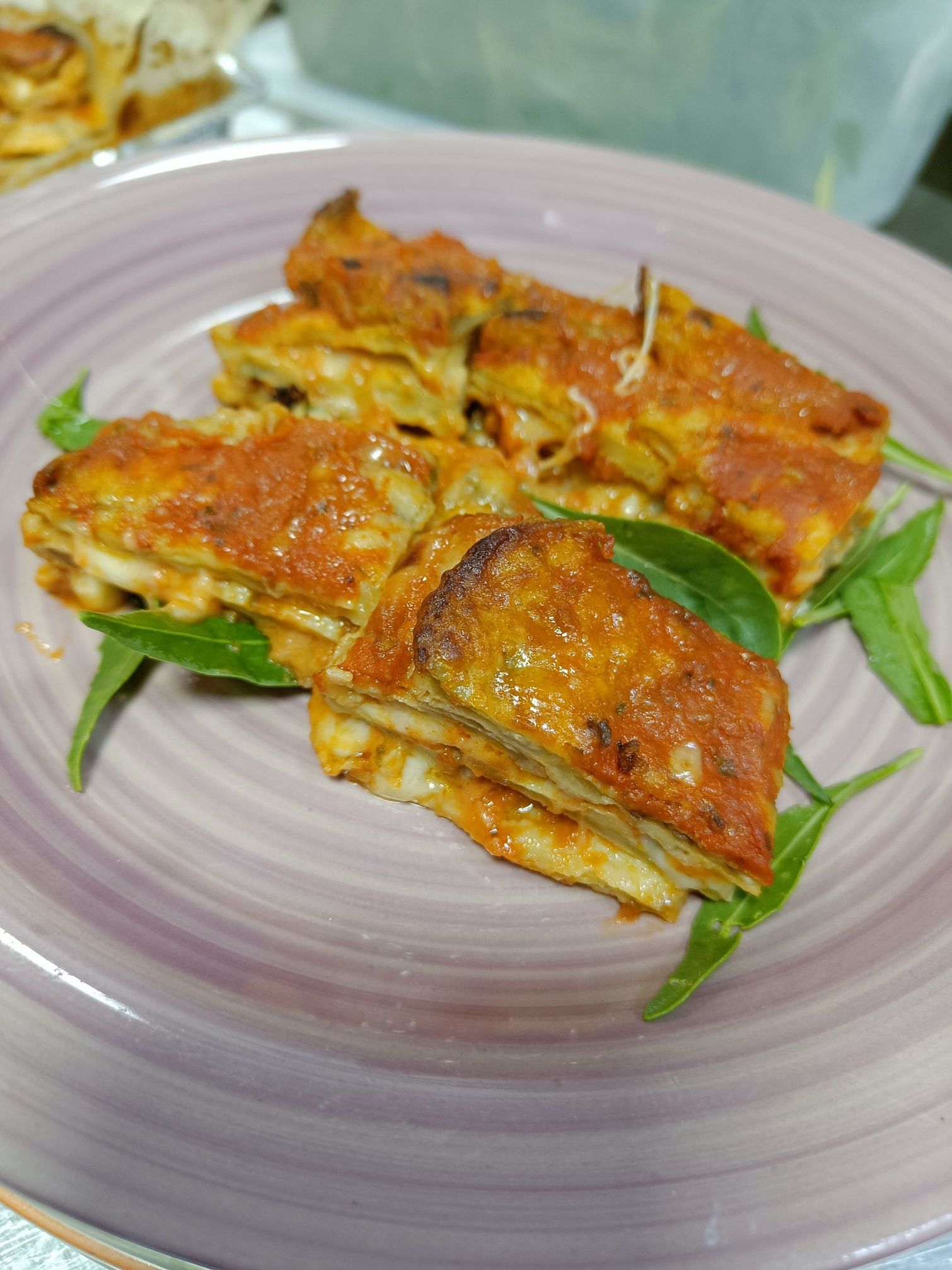 Rotoli di lasagna su un piatto viola con rucola e salsa rossa.