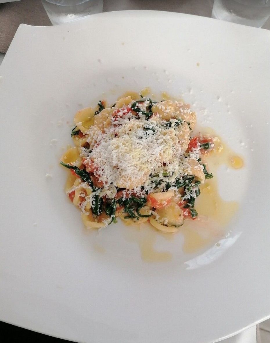 Piatto di pasta con pomodori, spinaci e formaggio grattugiato su un piatto bianco.