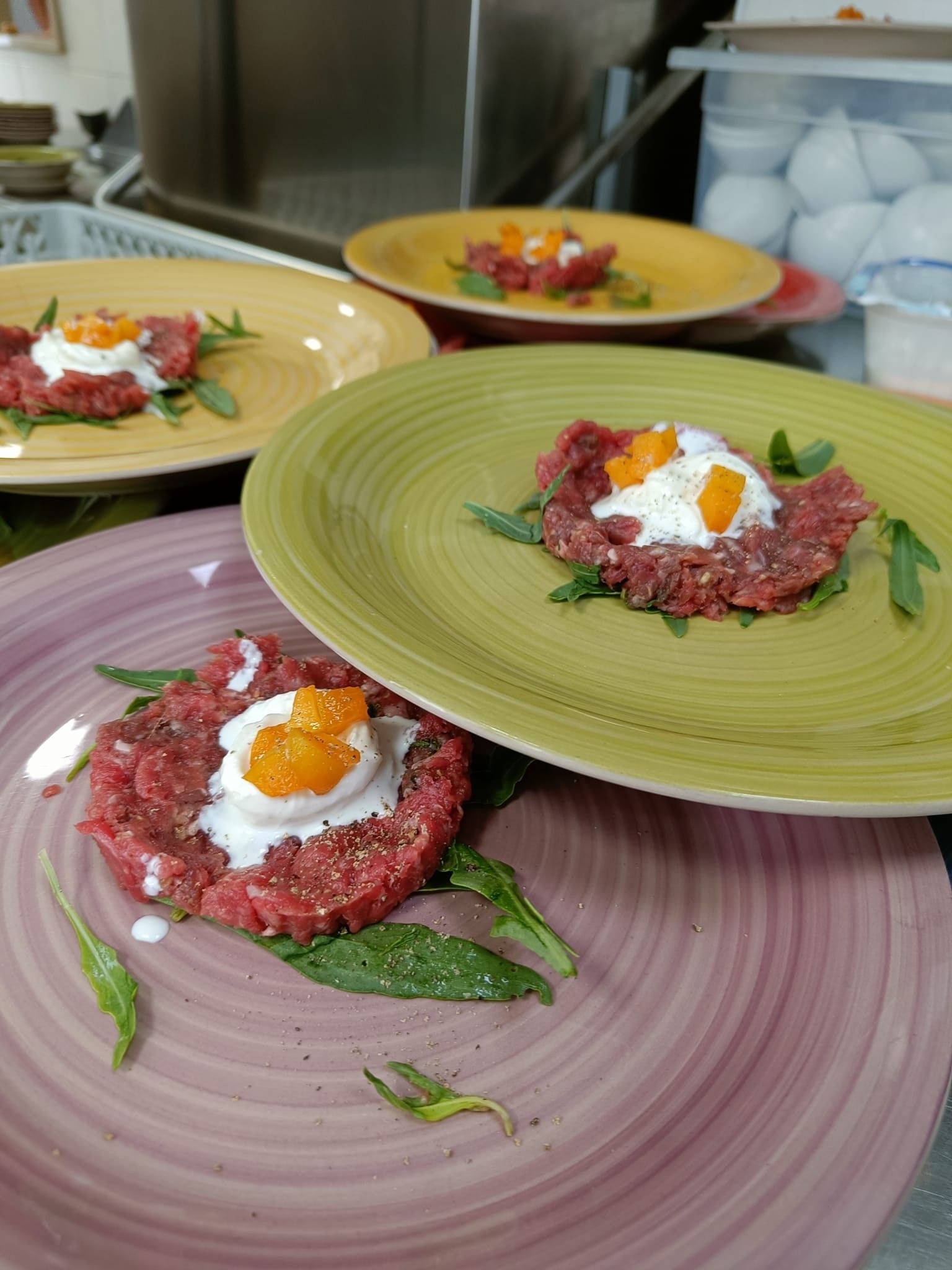 Piatti con tartare di carne cruda, guarnita con panna bianca e uova d'arancia. Presentati su piatti colorati.