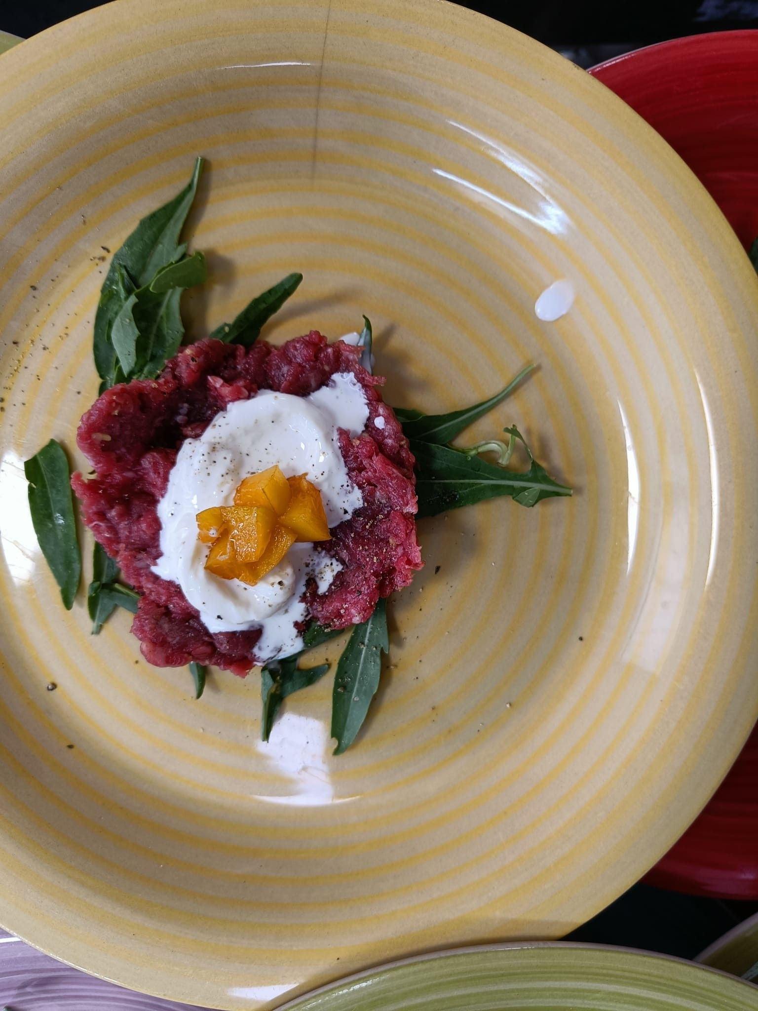 Tartare di manzo con salsa bianca e guarnizione su un piatto giallo.