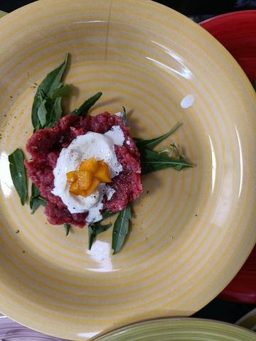 Tartare di manzo con salsa bianca e guarnizione su un piatto giallo.