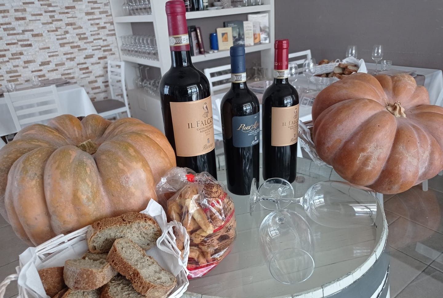 Zucche, bottiglie di vino, pane e bicchieri su un tavolo, ambiente interno.