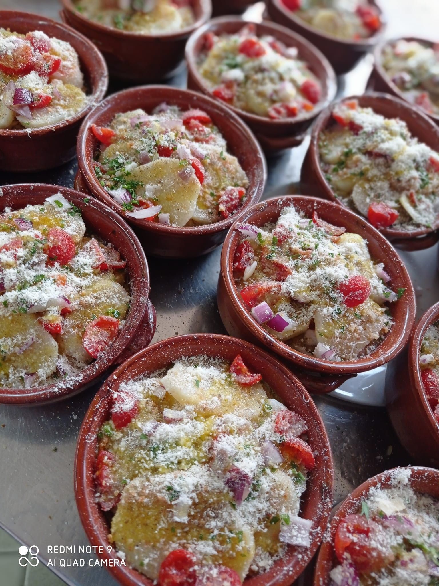 Piccoli piatti individuali di patate, conditi con pomodori, cipolle e formaggio grattugiato, in ciotole di ceramica marrone.