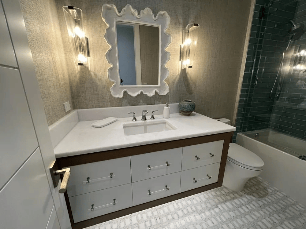 Bright bathroom with double vanity, lit mirror, white tile, and bathtub on the right.