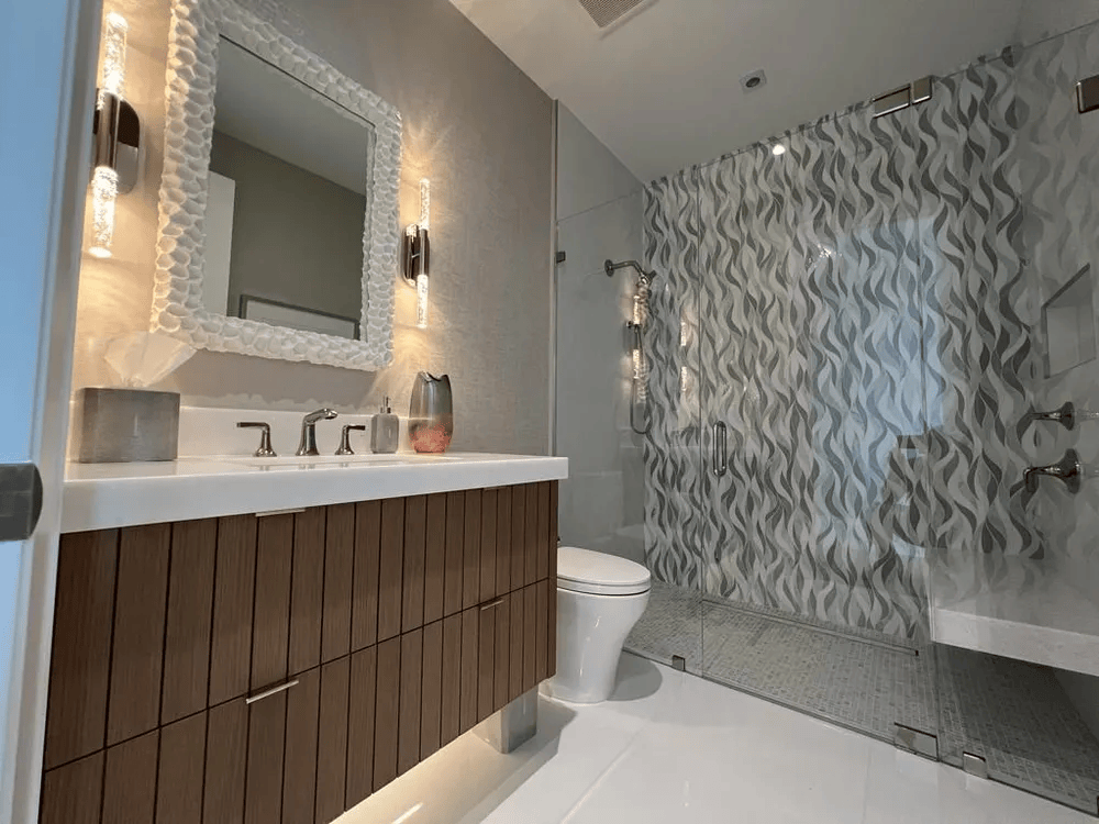 Modern bathroom with white vanity, lit mirror, toilet, and textured shower wall
