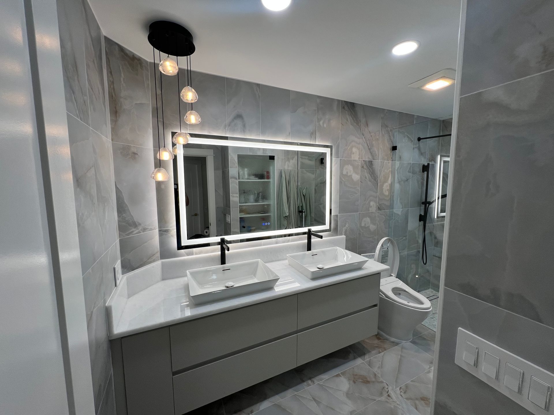 Modern bathroom with gray marble walls, double vanity, large mirror, and glass shower enclosure