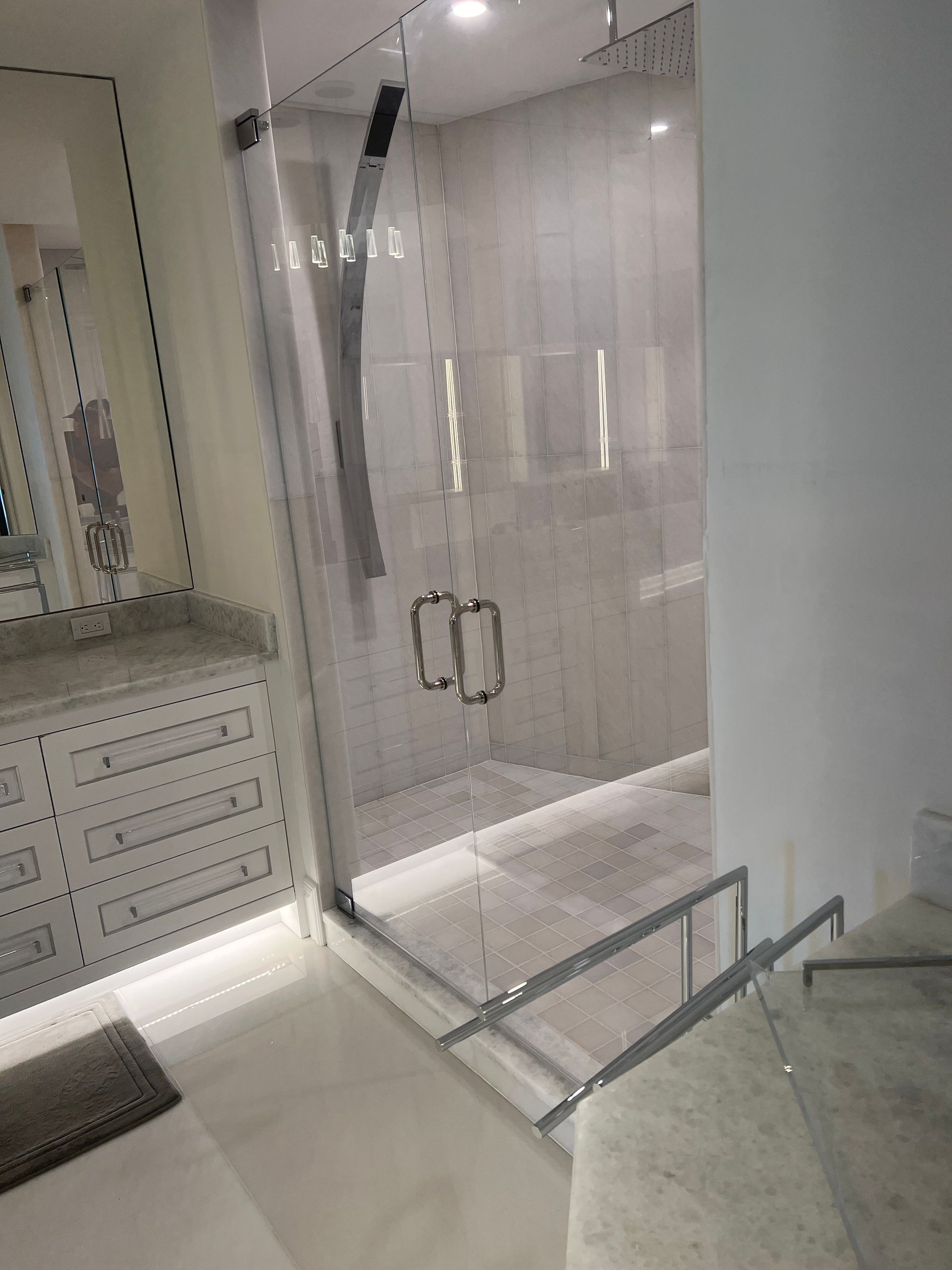 Modern bathroom with glass shower enclosure, white cabinetry, and marble countertop