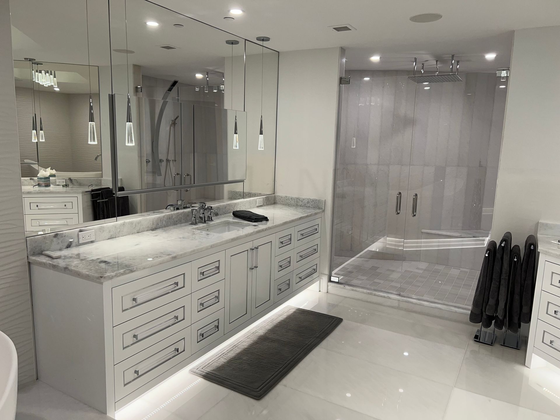 Modern white bathroom with double vanity, large mirror, walk-in shower, and glossy tile floor