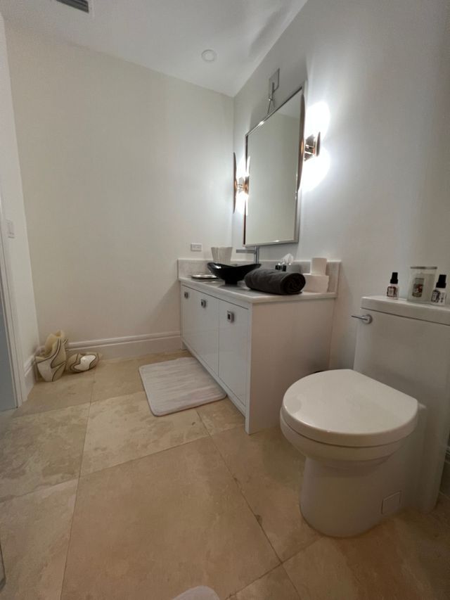 Modern bathroom with double sink vanity, mirror, toilet, and beige tile floor