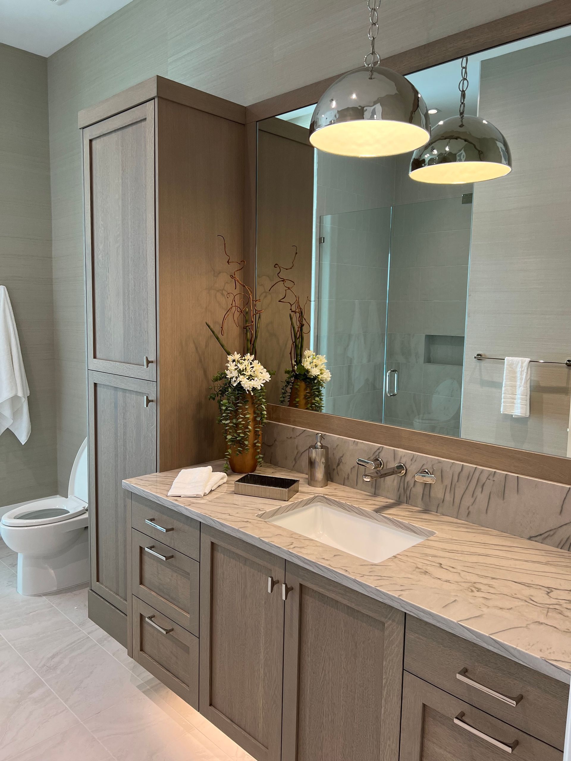 Modern bathroom vanity with wood cabinets, double sink, pendant lights, and a glass shower in the background