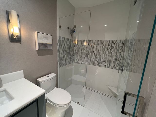 Modern bathroom with toilet, vanity sink, glass shower, and gray tile accents.