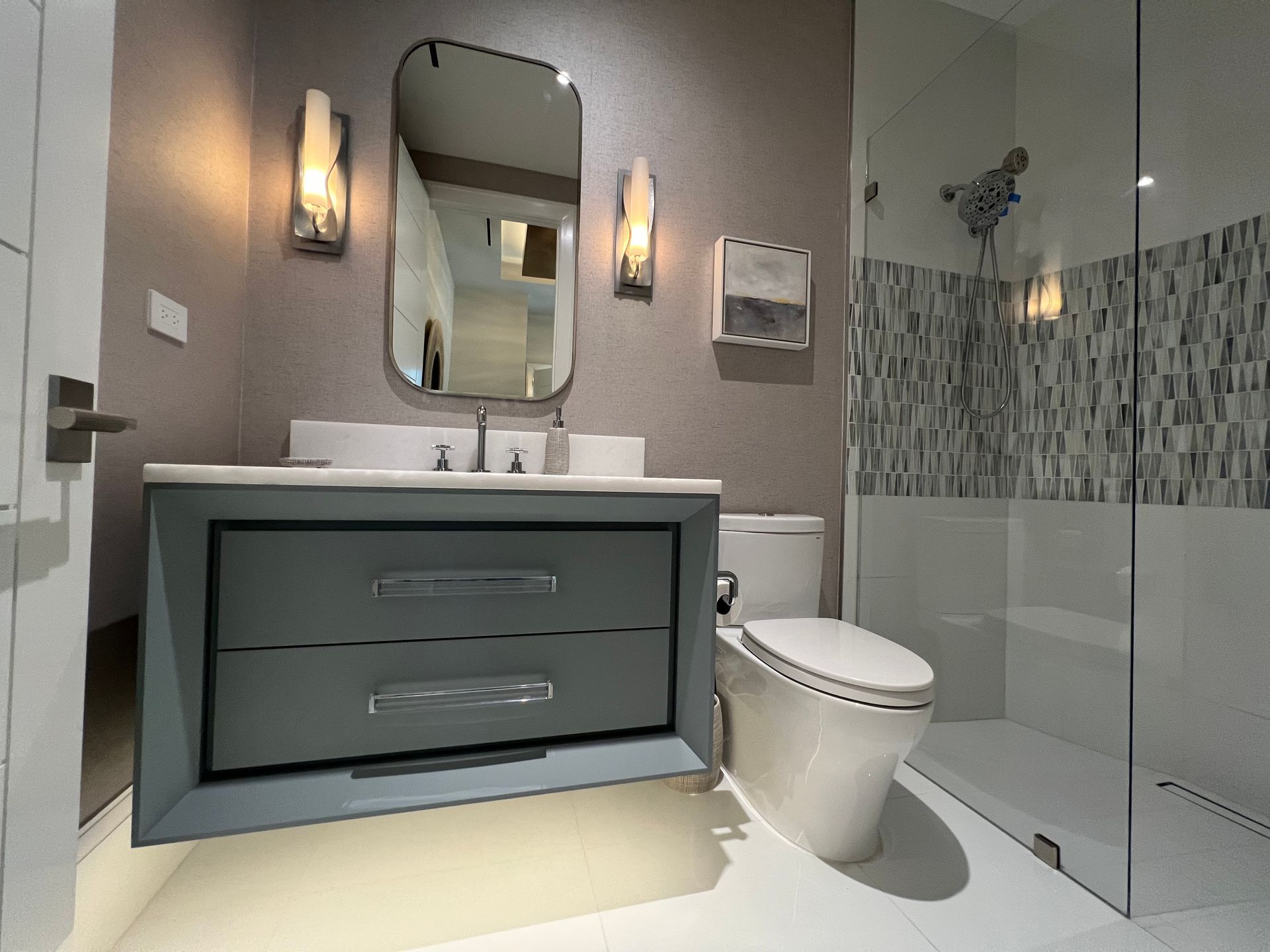 Modern bathroom with gray vanity, mirror, wall sconces, toilet, and glass shower enclosure