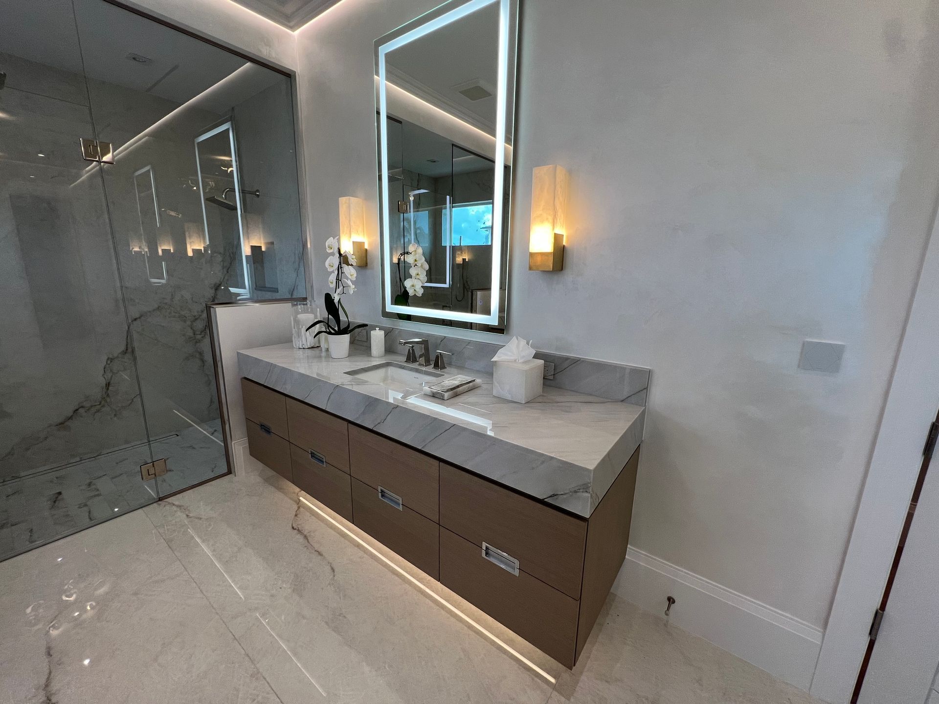 Modern bathroom vanity with double sinks, large mirror, wall sconces, and glass shower enclosure