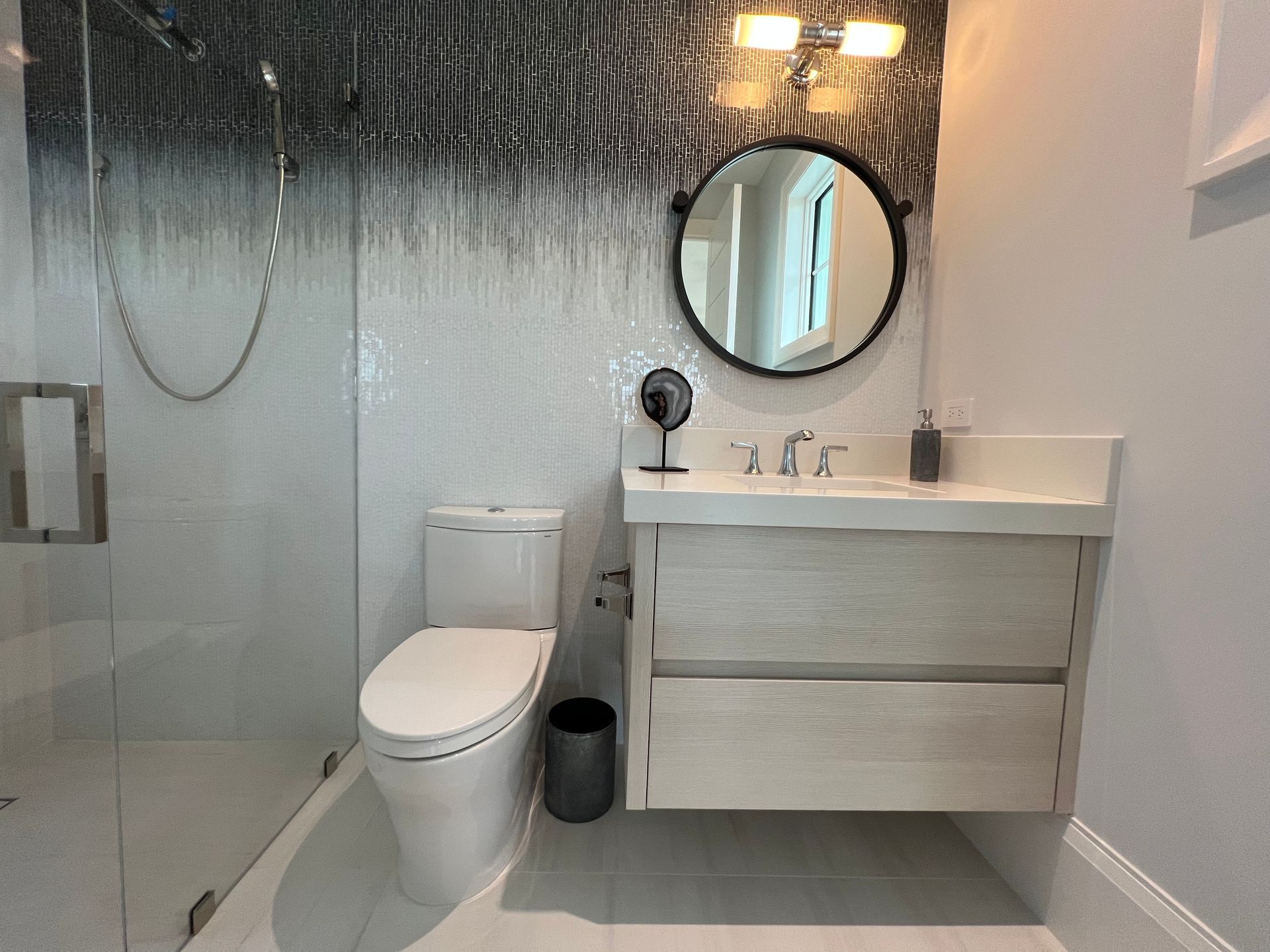 Modern bathroom with glass shower, toilet, and floating vanity with round mirror.