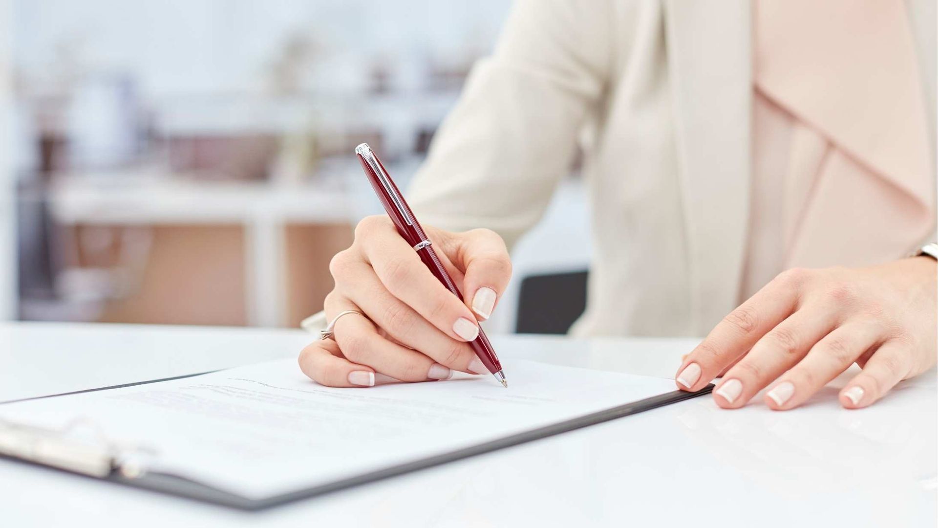 Hands writing in a notebook with a pencil at a bright desk