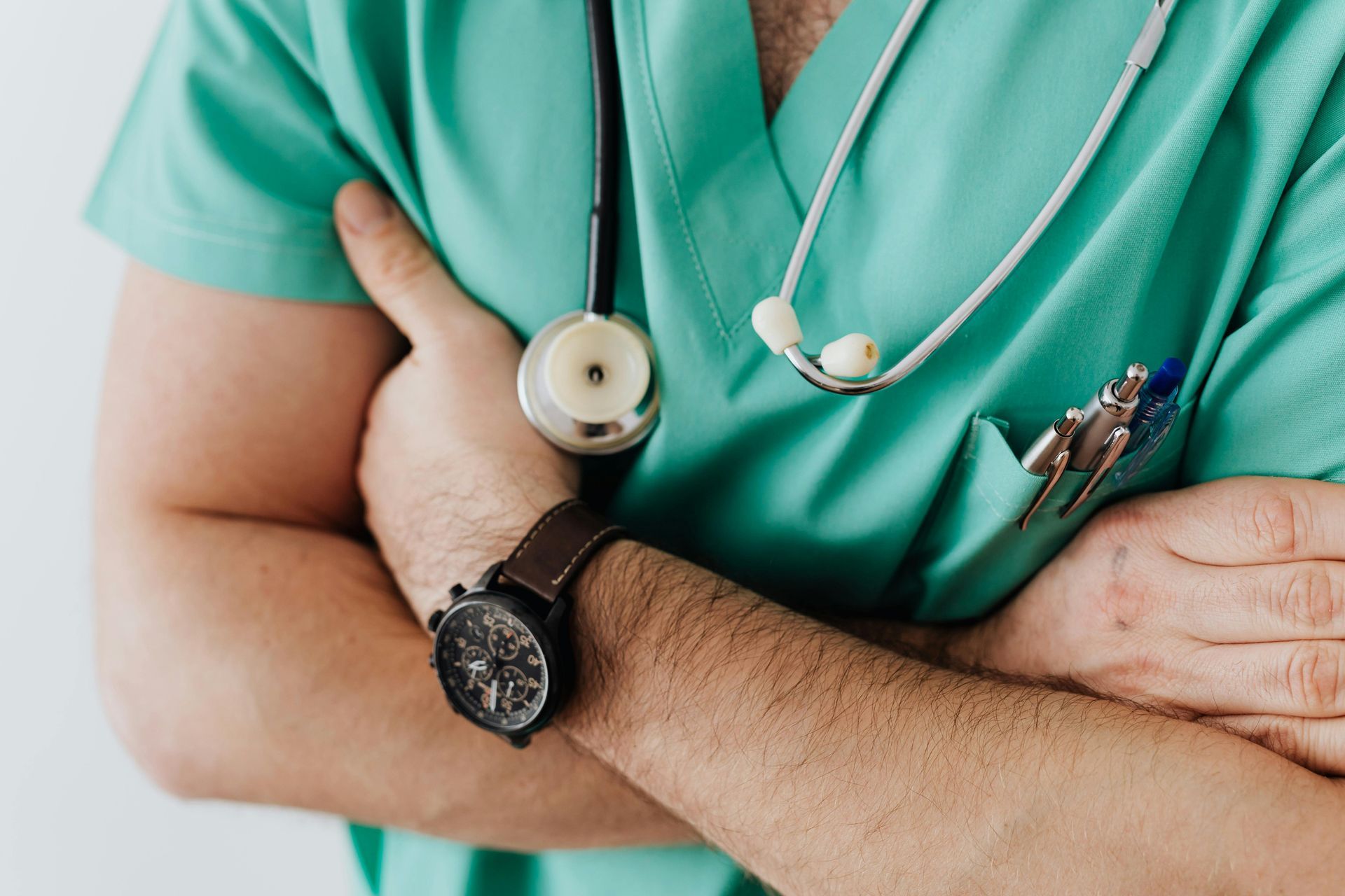 Healthcare worker in teal scrubs with arms crossed, wearing a stethoscope and wristwatch