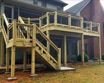 A wooden deck with stairs leading up to it is in front of a house.