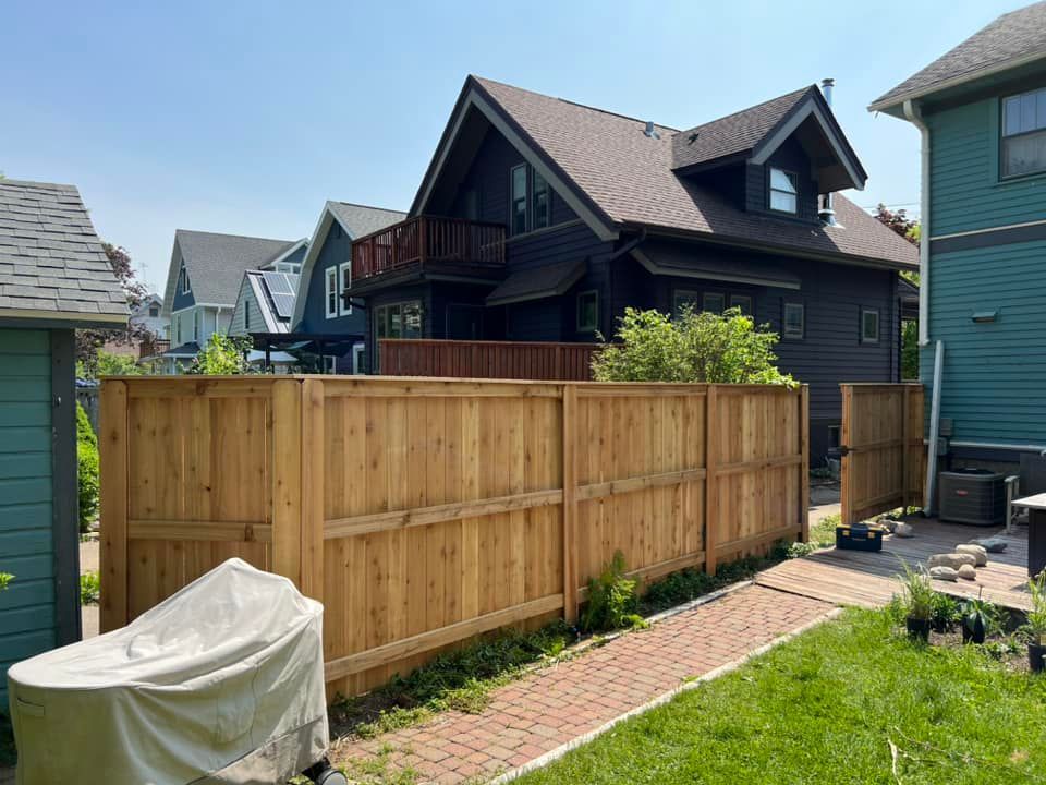 Wooden fence in backyard with brown siding house and blue house in the background on a sunny day.