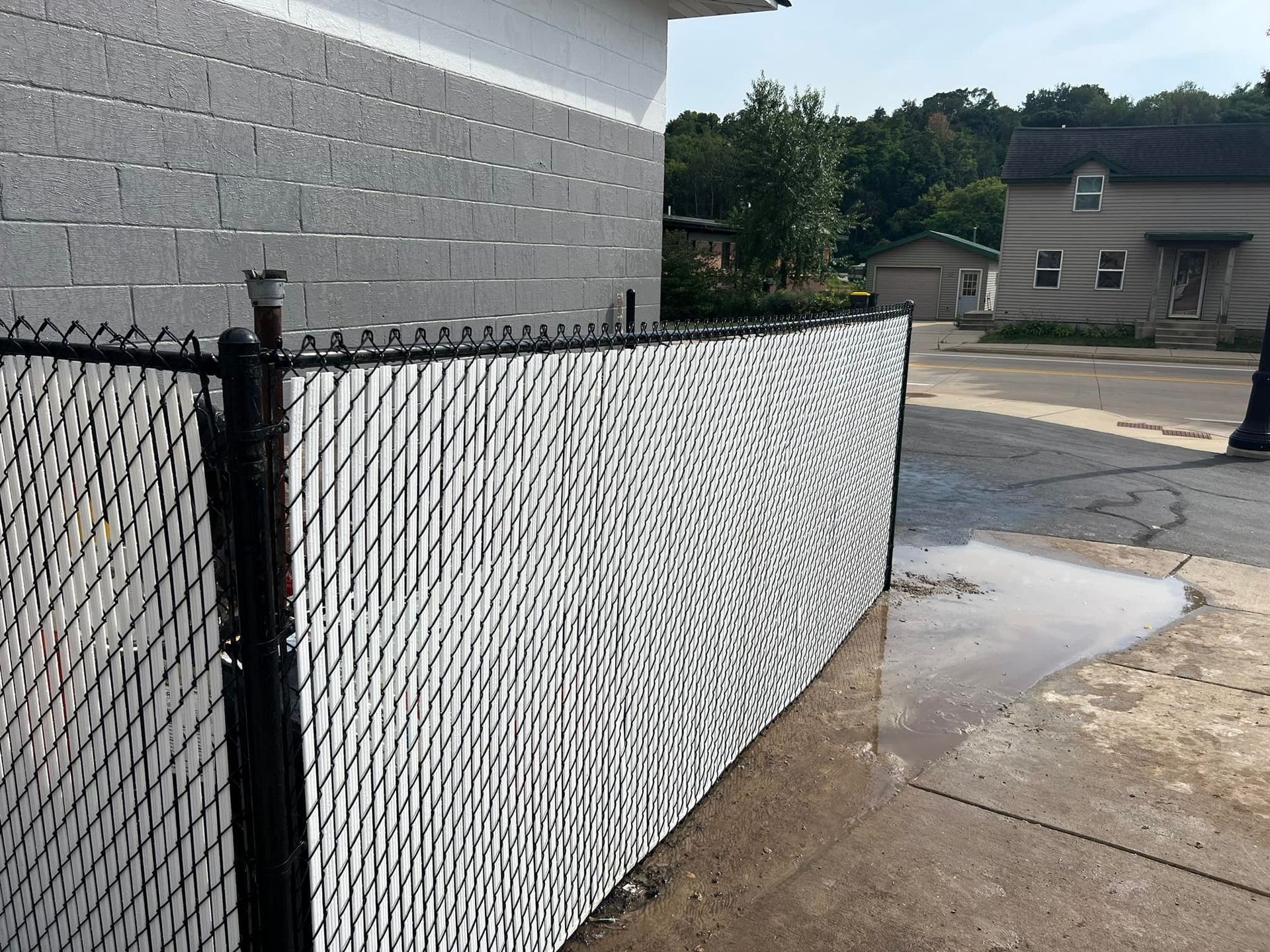 Black chain-link fence with white privacy slats next to a gray brick building.