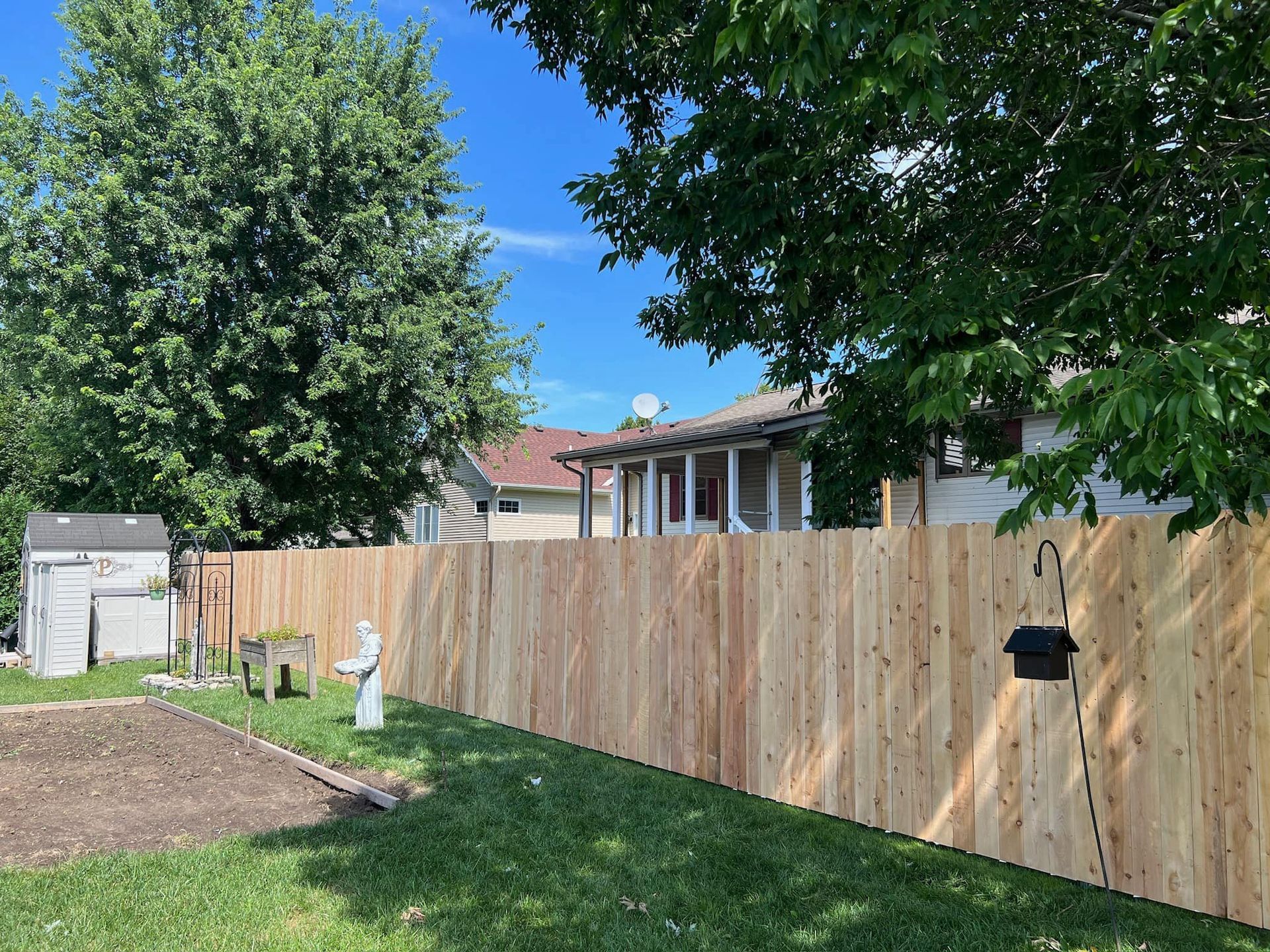 Wooden fence in a yard with a house in the background, green grass and trees.
