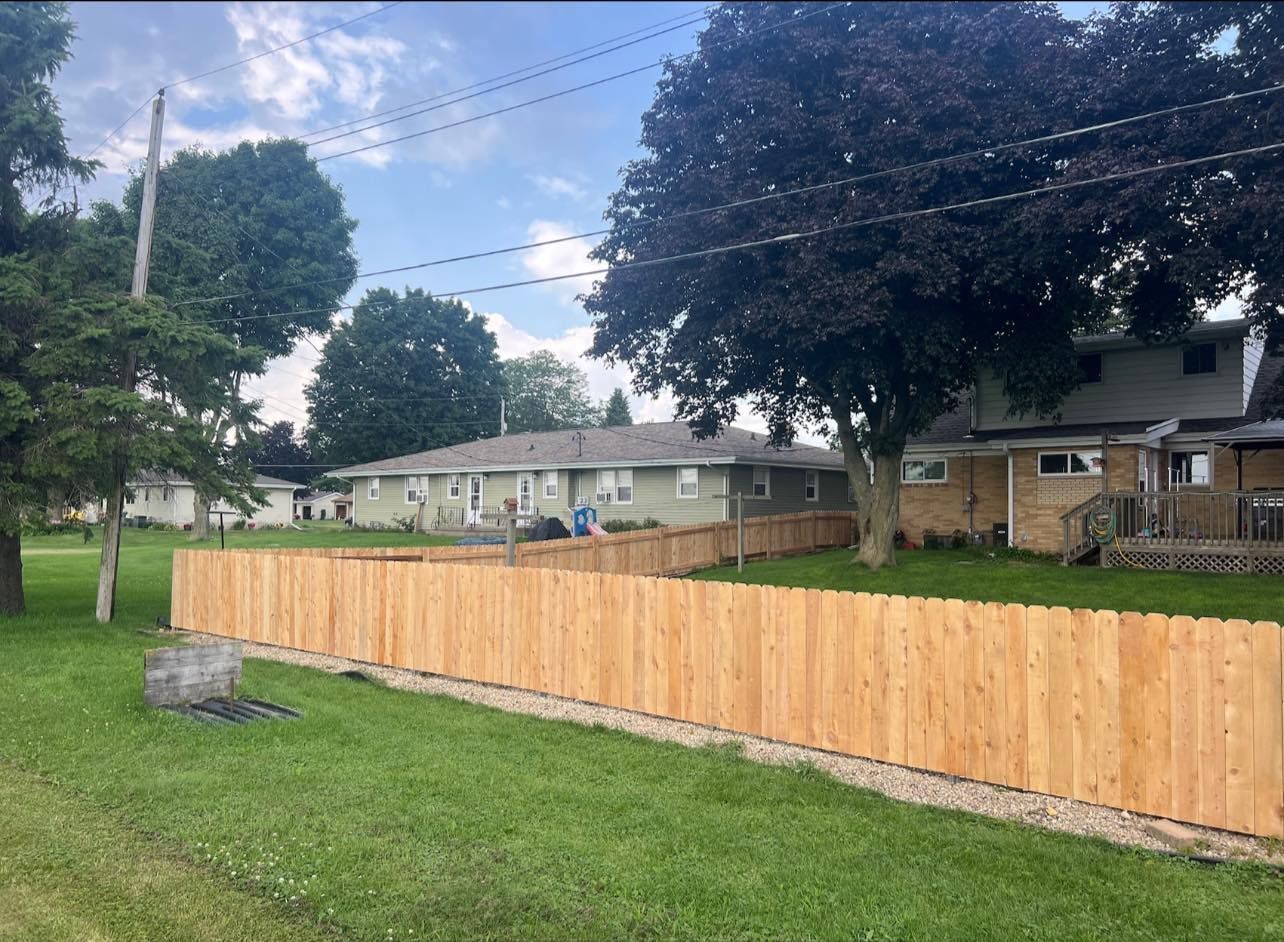 Wooden fence in front of a row of houses on a grassy lawn, under a cloudy sky.