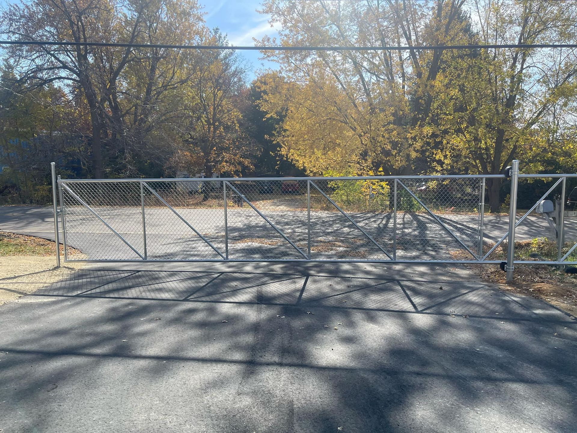 Chain link gate across paved driveway, trees in the background.