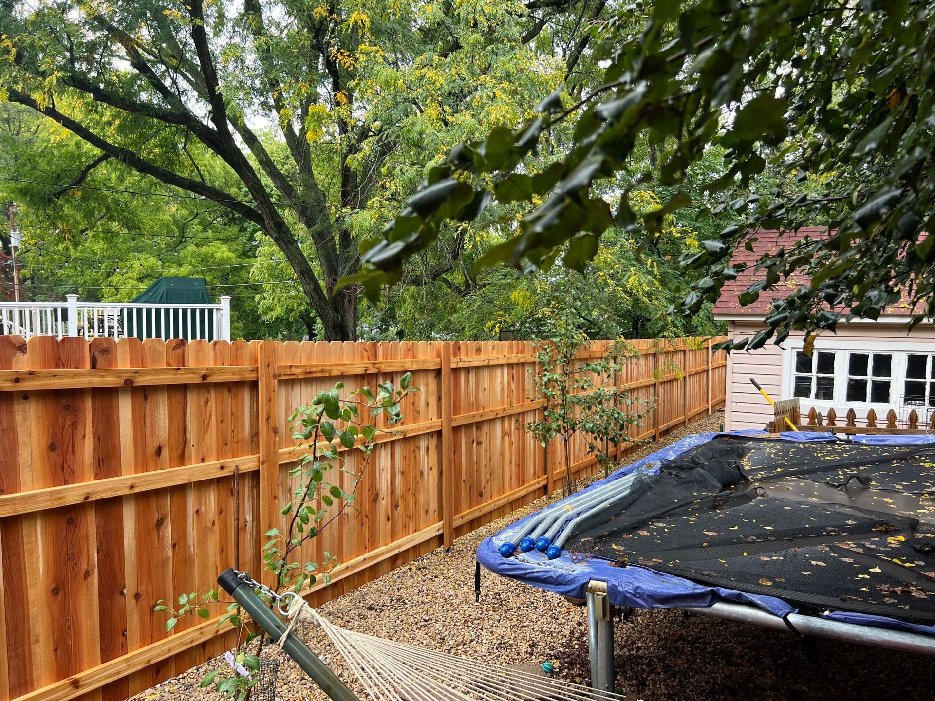 Wooden fence in a backyard, with a trampoline and trees in the background.