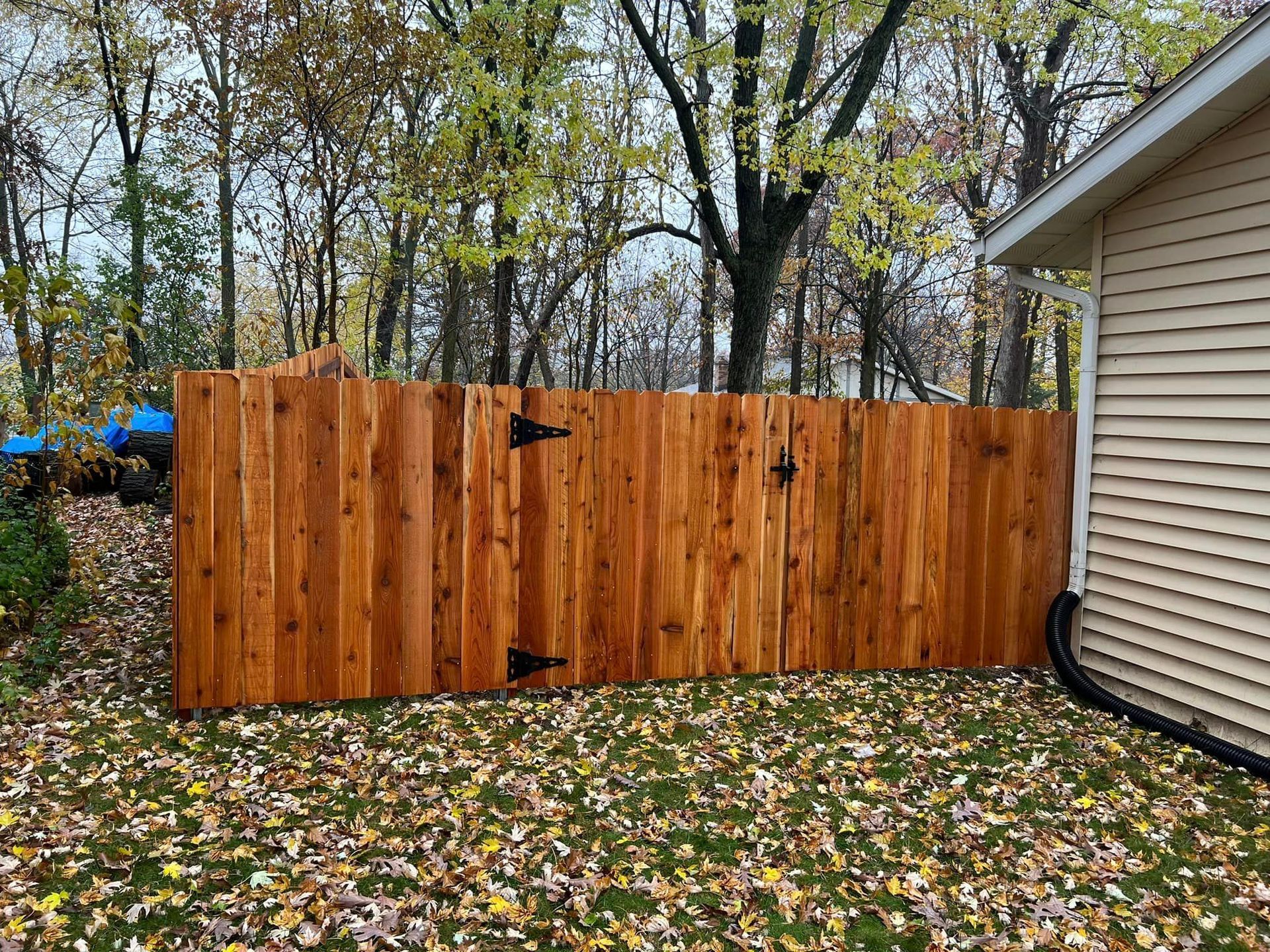 Wooden fence, stained brown, in a backyard setting, next to a house with tan siding.