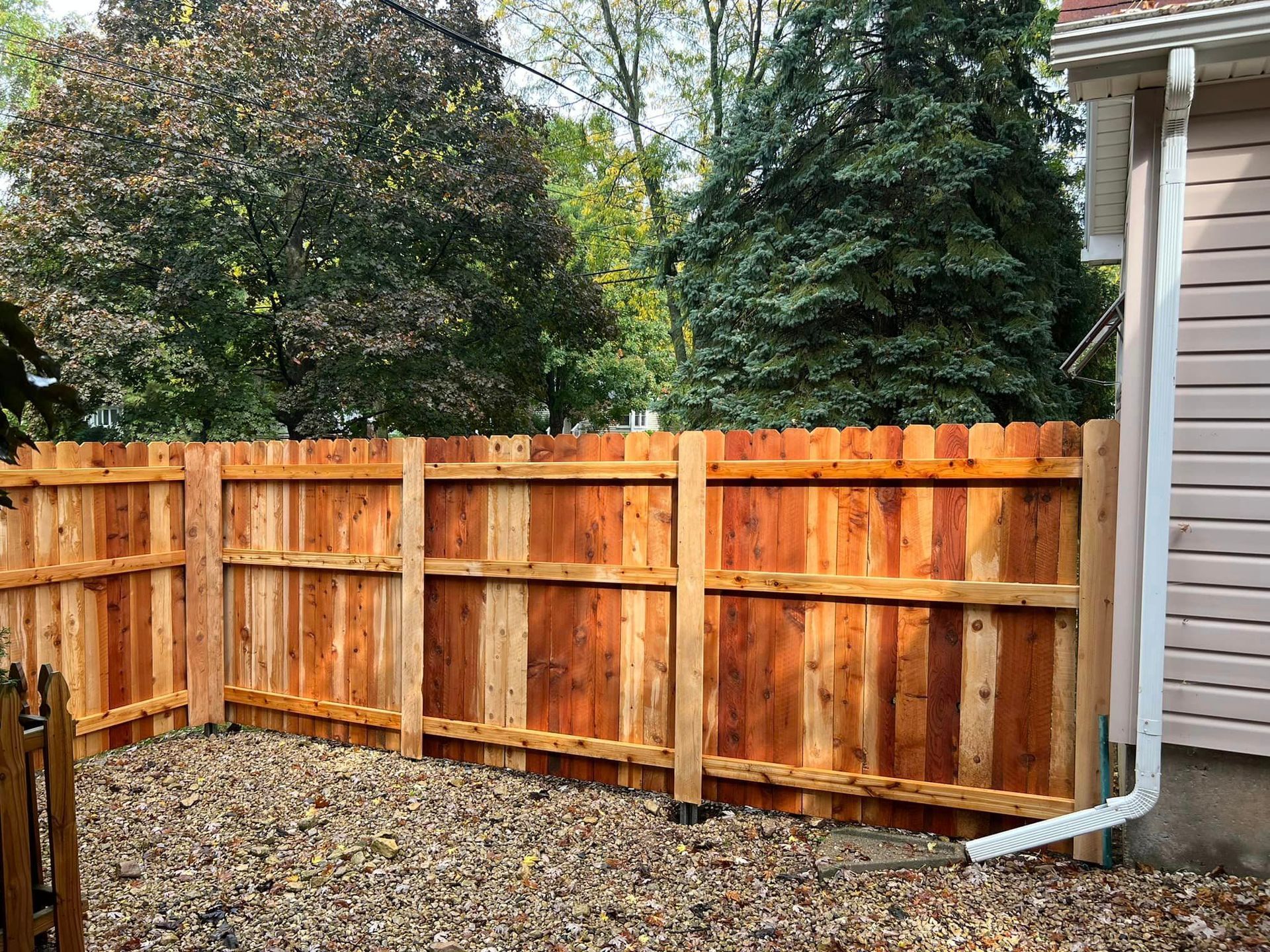 Wooden fence, light brown color, adjacent to a beige house, with a white gutter.