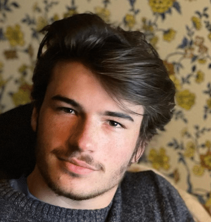 Young man with dark hair and a slight smile against a floral backdrop.