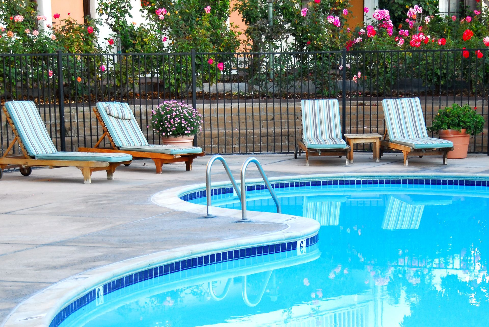 Poolside scene with lounge chairs, blue water, and flowers.