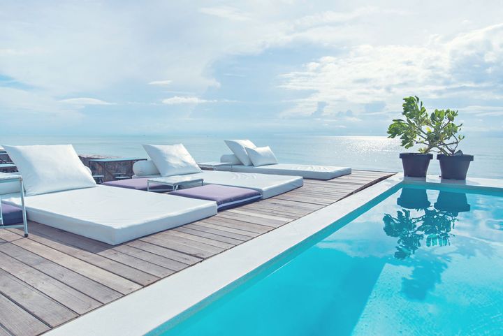A swimming pool surrounded by chairs and a wooden deck overlooking the ocean.