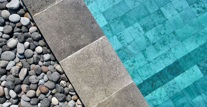 A swimming pool surrounded by rocks and tiles with a turquoise water.