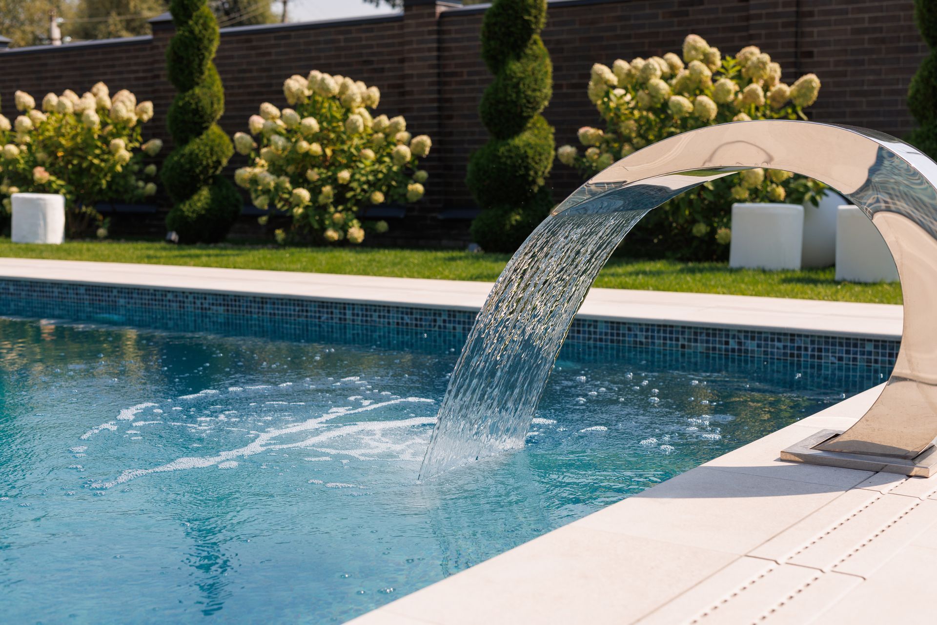 Pool with a curved waterfall feature, surrounded by greenery and landscaping.
