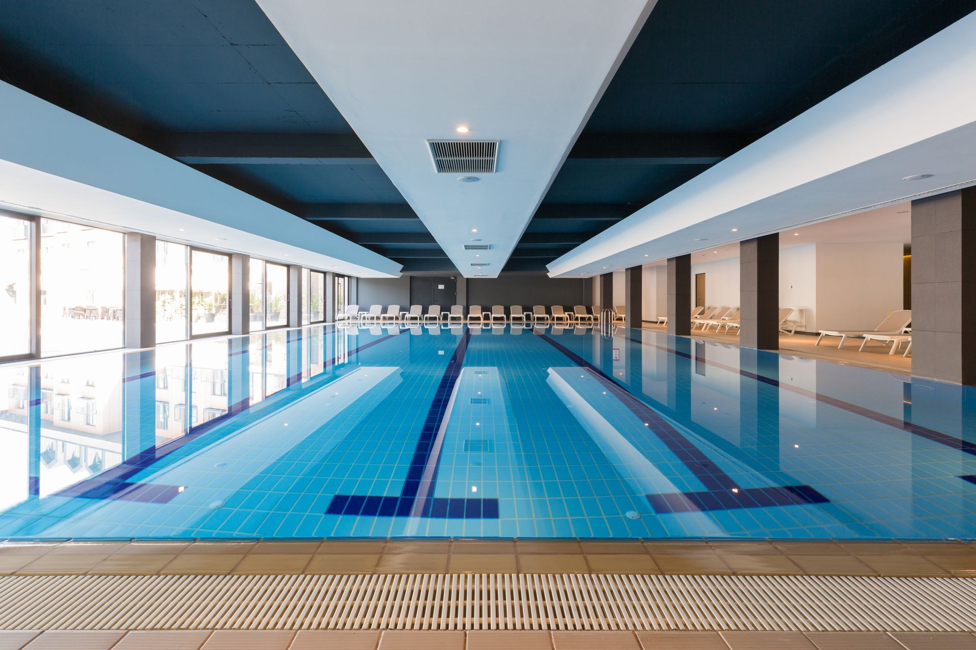 Indoor swimming pool with blue water, lane markers, and seating along the sides.