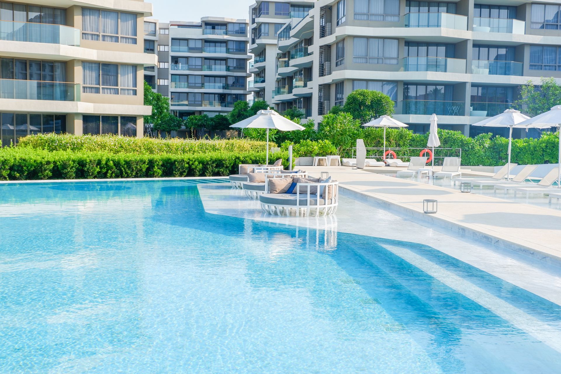 Swimming pool with lounge chairs and umbrellas, surrounded by apartment buildings.