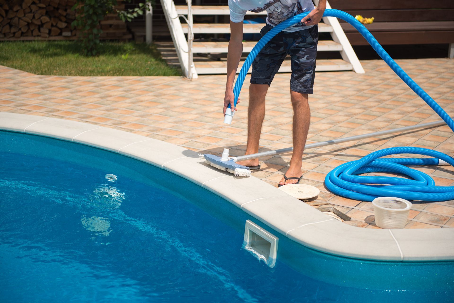 Person cleaning a blue swimming pool with a vacuum hose and brush.