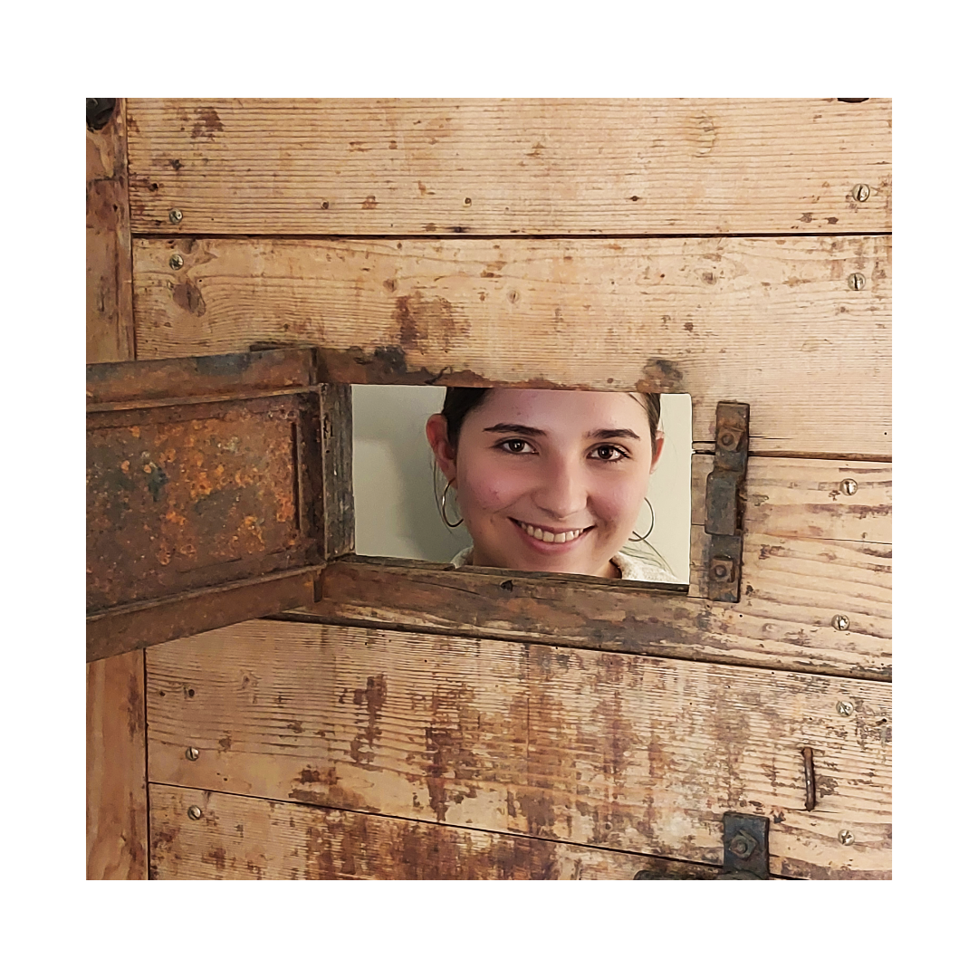 Eine Frau lächelt durch ein Loch in einer Holzwand.