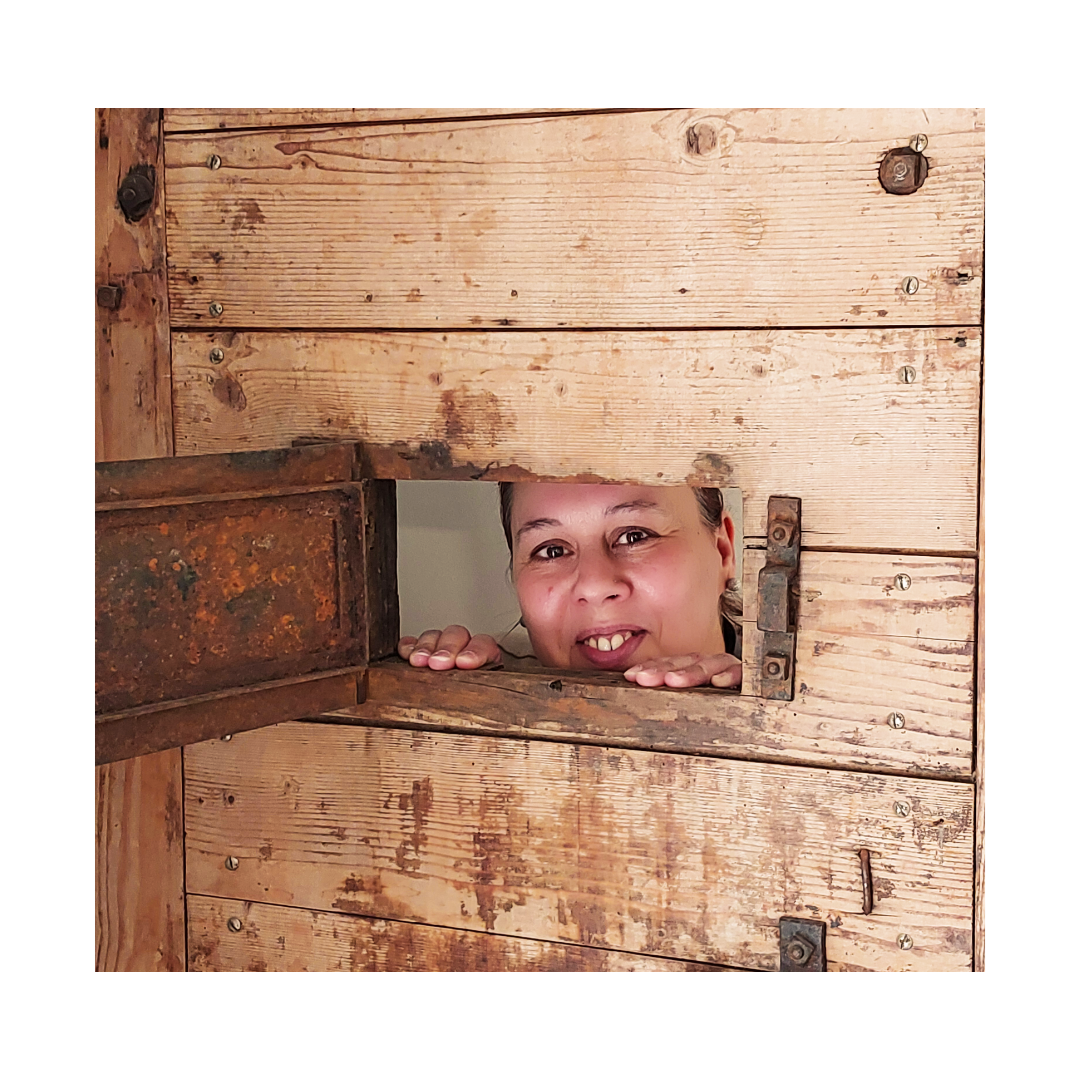 Eine Frau guckt aus einem Loch in einer Holzwand.