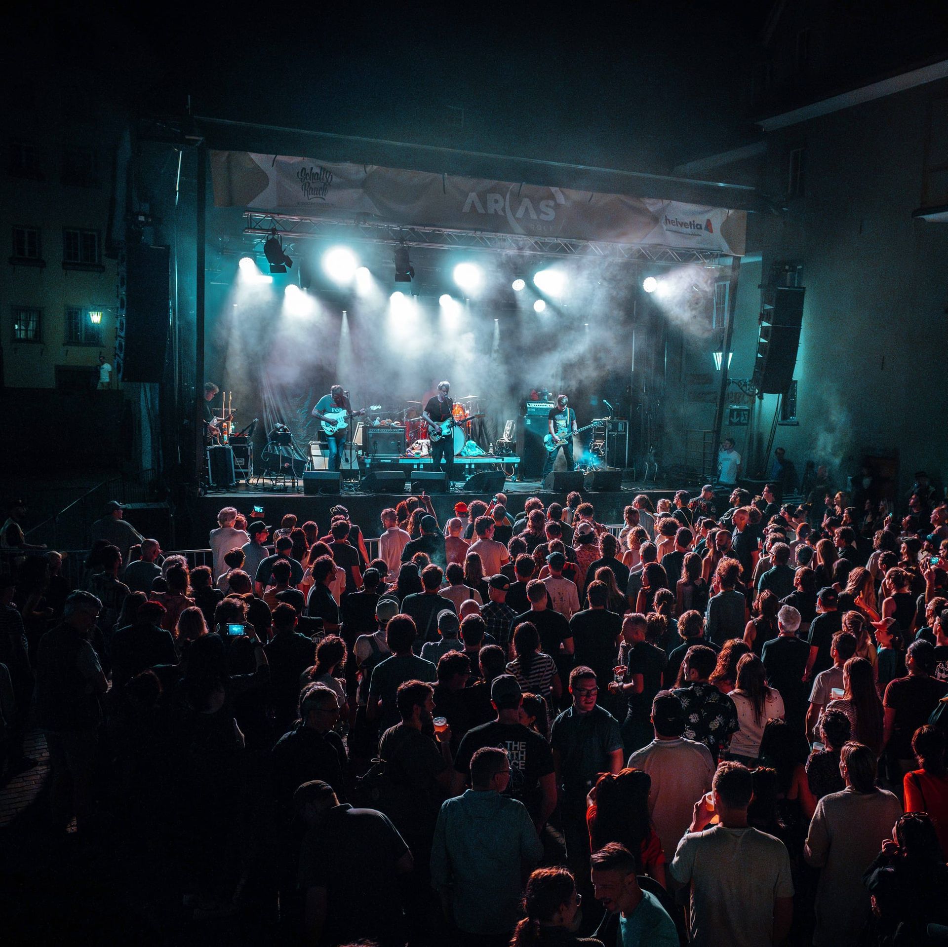 Crowded concert hall with a band onstage under blue spotlights and a cheering audience