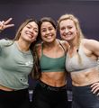 A woman is holding a kettlebell on her shoulder and smiling.