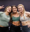A woman is holding a kettlebell on her shoulder and smiling.