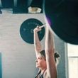 A woman is lifting a barbell over her head in a gym.