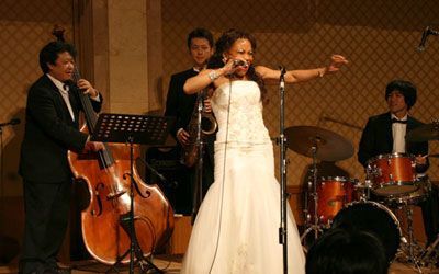 A woman in a white dress is singing into a microphone in front of a band.