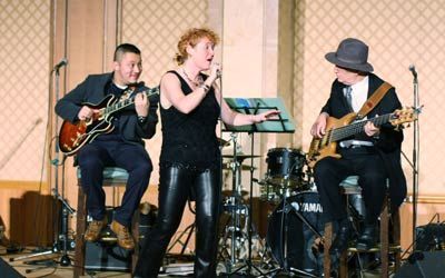 A woman is singing into a microphone while two men play guitars on stage.