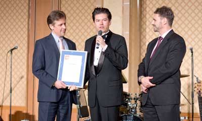 Three men in suits are standing next to each other on a stage holding a certificate.