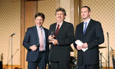 Three men in suits and ties are standing next to each other on a stage holding microphones.