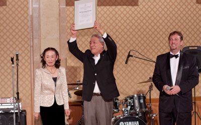 A man in a tuxedo is holding a certificate in front of a drum set.