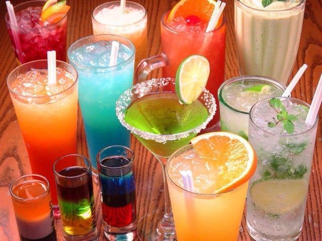 Various colorful cocktails and shots on a wooden surface, including orange, blue, and green drinks with fruit garnishes.