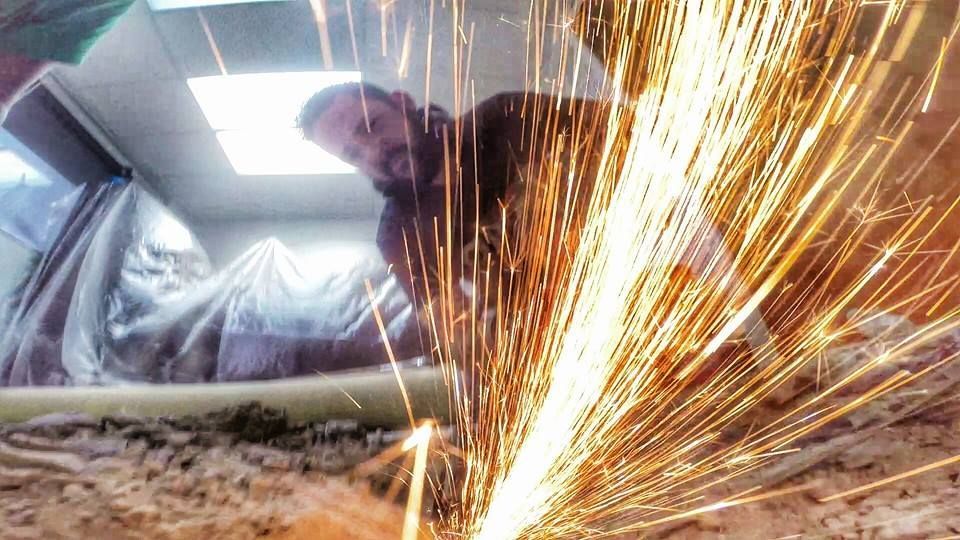 A man is grinding a piece of metal with sparks coming out of it.